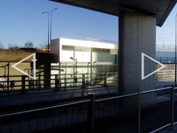 Two photos taken from underneath a protruding bit of the Westfield London shopping centre automatically stitched together showing the London Overground station across the street. You can just see the Overground roundel on the platform (December 2008)